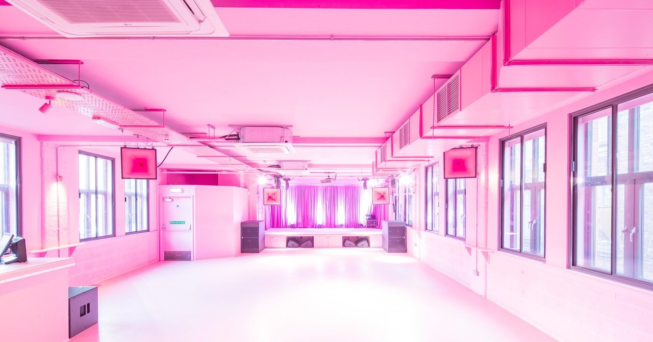 A bright pink warehouse style room with a stage at the far end